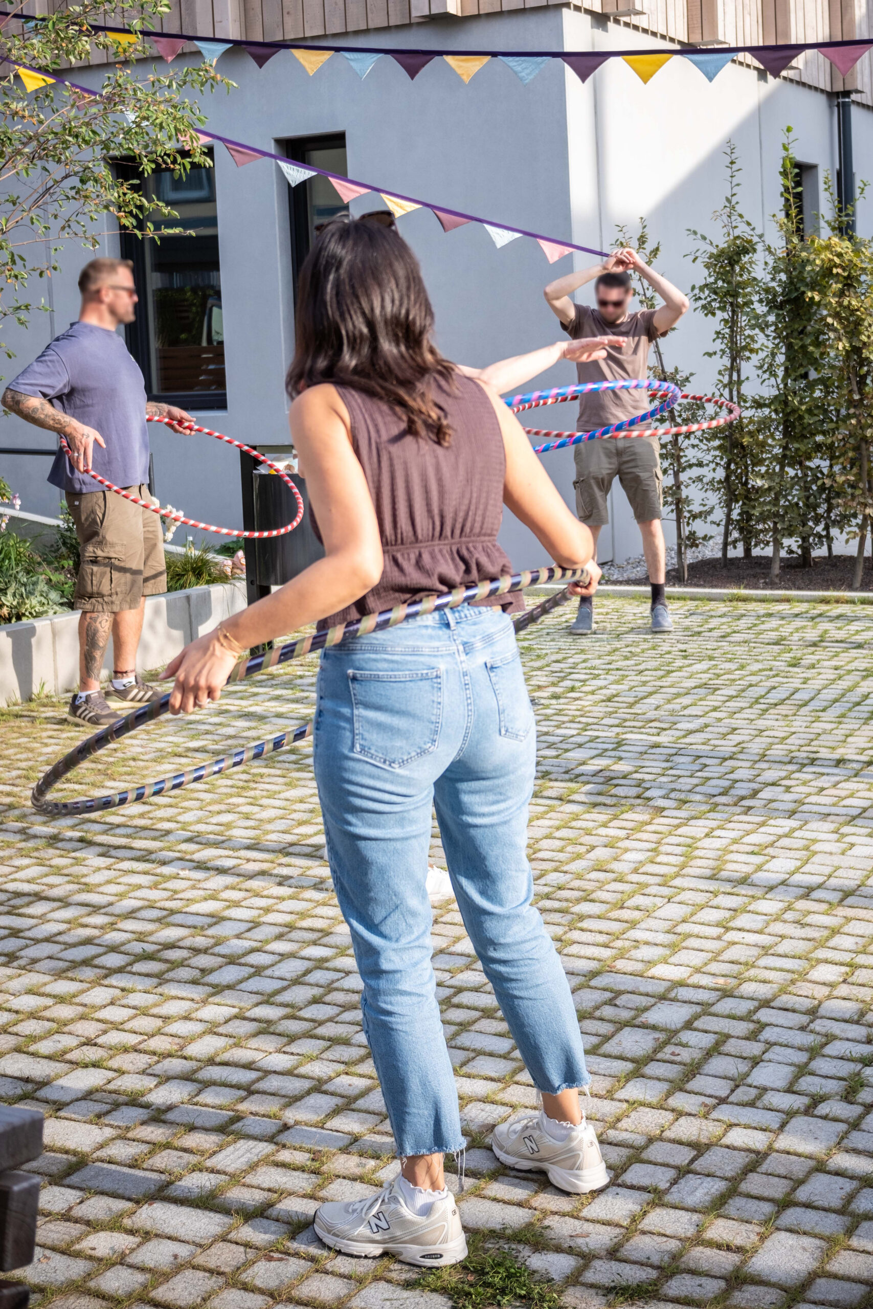 Eine Frau beim Hula Hoop im Freien, weitere Personen mit Reifen im Hintergrund.